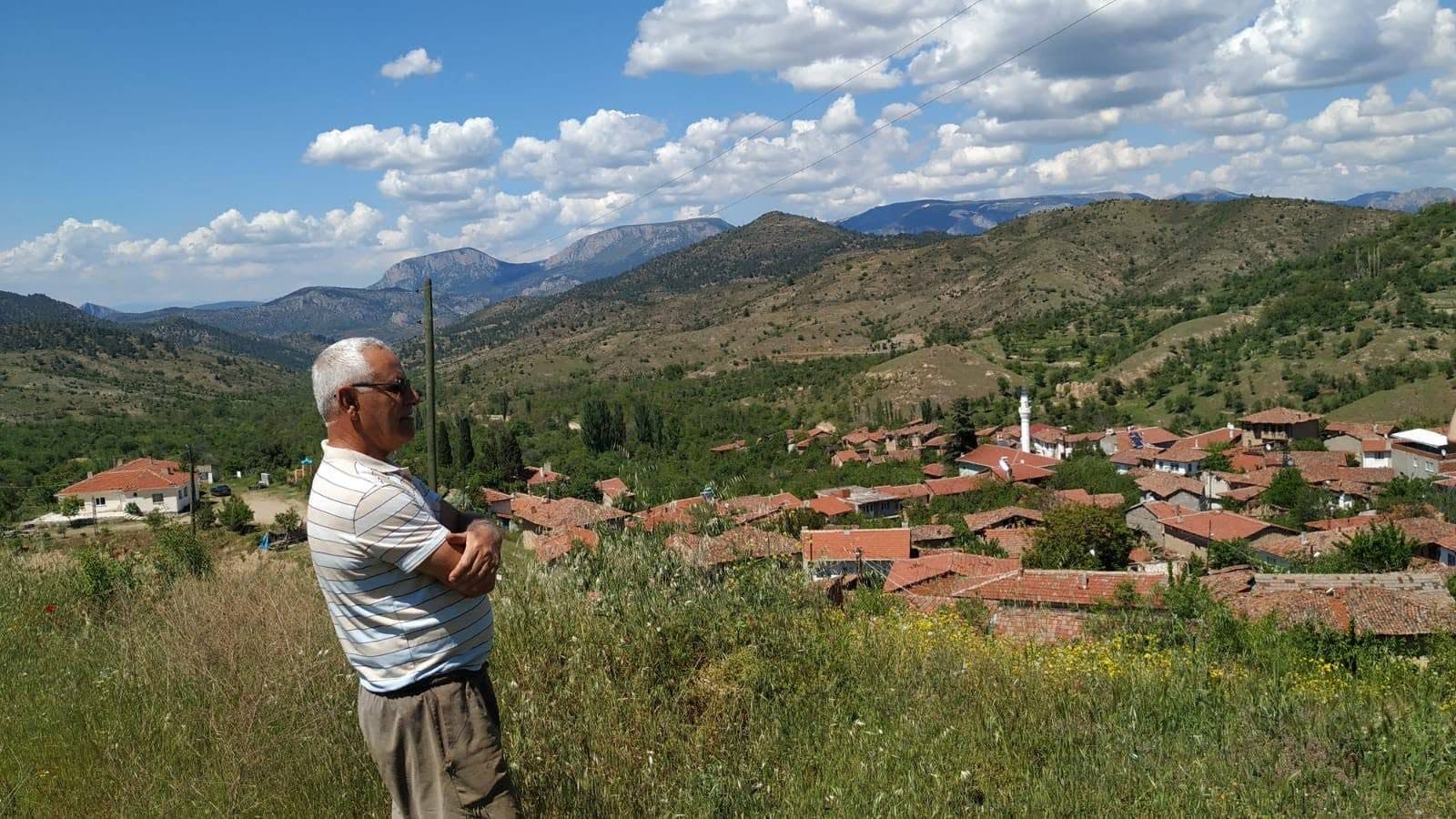 Arıcı, çayırın kenarından köyü ve karşıdaki dağları izliyor